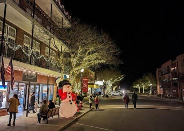 Una calle de noche con un gran decorado de muñeco de nieve, gente caminando y edificios con letreros.