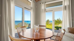 Een ronde houten tafel met stoelen, een kandelaar van glas en uitzicht op de oceaan door grote ramen.