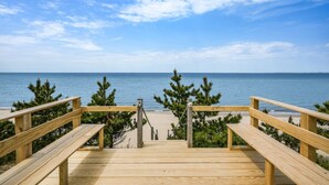 Een houten terras dat naar een strand leidt, met een helder uitzicht over de oceaan en een zandkust.