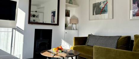 A living room with a sofa, a coffee table with fruit, a fireplace, and a bookshelf.