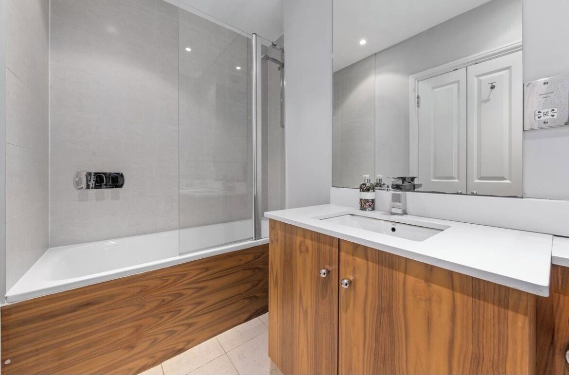 A modern bathroom with a glass shower enclosure, a wooden vanity with a sink, and a large mirror above the vanity.