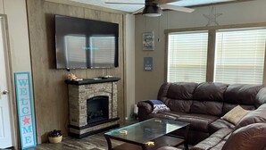 A living room with a stone fireplace, leather sofa, and a flat-screen TV mounted on the wall.