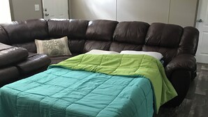 Un salon avec un canapé d’angle, une couvre-lit verte et turquoise, et un plancher en bois.