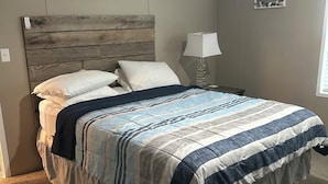 A bedroom with a wooden headboard, a bed with a striped bedspread, a bedside lamp, and a small picture on the wall.