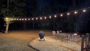 An outdoor seating area with a fire pit, string lights, and a covered grill.