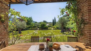 Et træbord med udsigt til en velplejet have, en murstensmur og en pergola med slyngplanter.