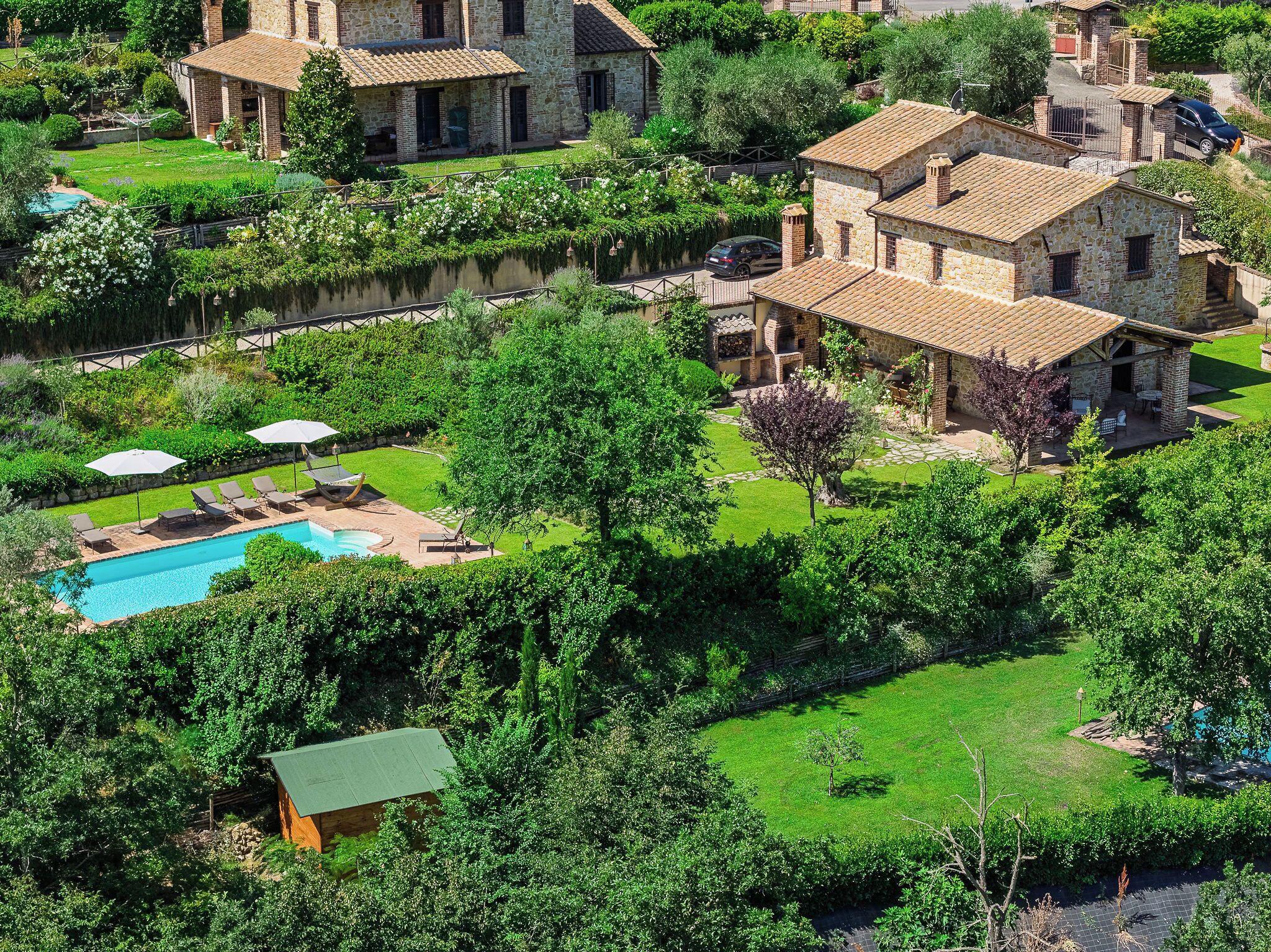 A large stone house with a swimming pool, surrounded by lush greenery and a small wooden structure.