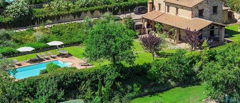 A large stone house with a swimming pool, surrounded by lush greenery and a small wooden structure.