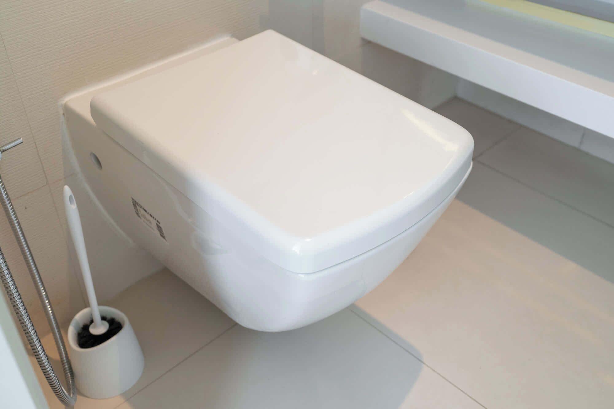Eine weiße Toilette in einem Badezimmer mit weißem Boden und einer weißen Badewanne im Hintergrund.