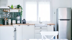 Una cucina moderna con mobili bianchi, un frigorifero in acciaio inossidabile, una finestra con persiane e un piano di lavoro in legno.