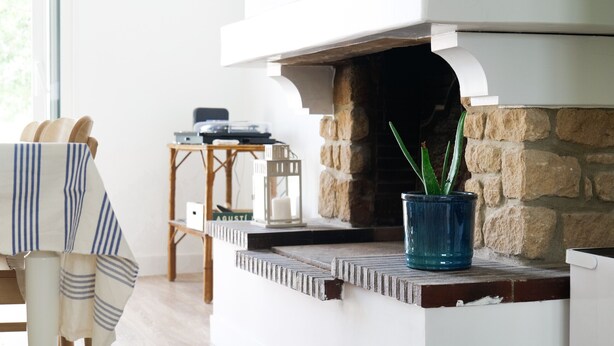 Un caminetto con rivestimento in pietra, un vaso blu con una pianta e un tavolo di legno con una lanterna.