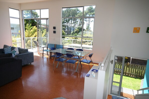 Relax in this inviting living area with a sofa set, dining table, and kitchenette, leading to a balcony with a garden view.