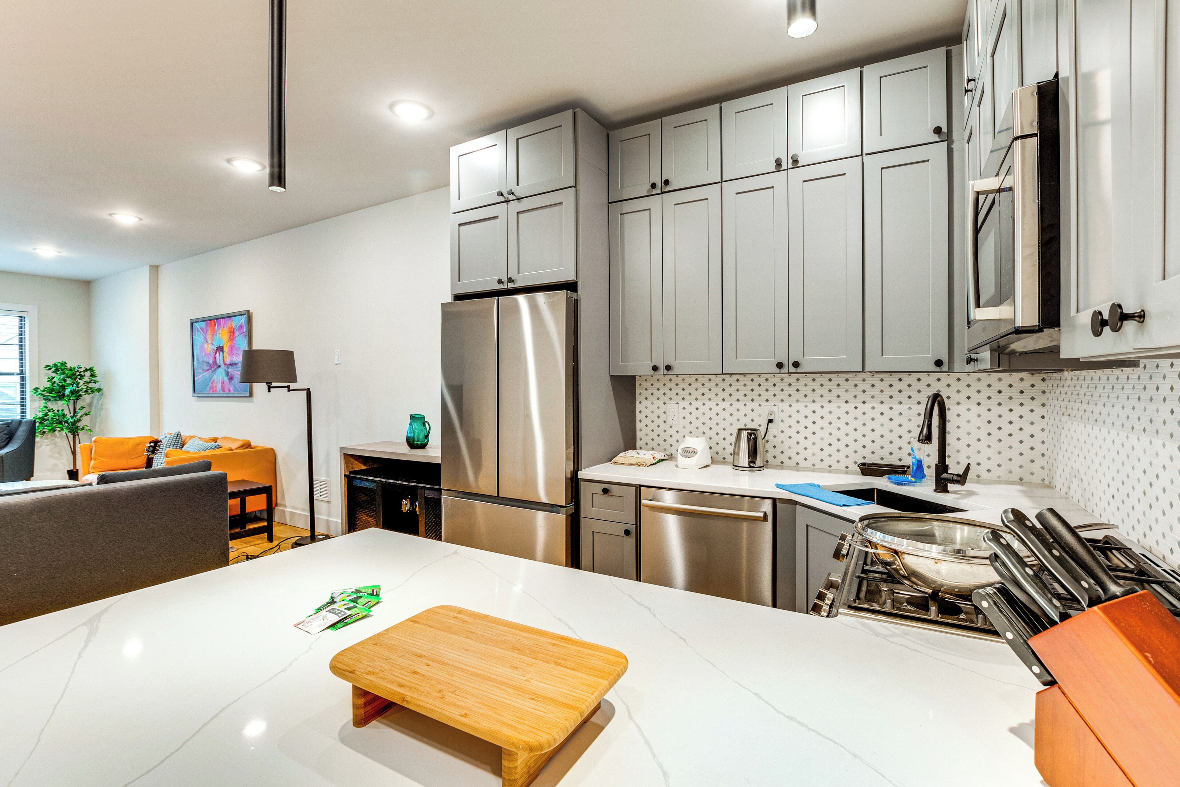 A modern kitchen with stainless steel appliances, grey cabinets, and a white countertop.