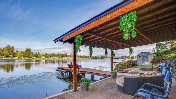 Un patio junto al lago con una terraza de madera, zona de estar y un cobertizo pequeño.