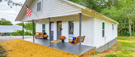 A white single-story house with a porch, a swing chair, and a small garden with orange flowers.