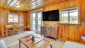 A wooden cabin interior with a dining area, a TV mounted on the wall, and large windows offering views of the outdoors. - Lake WI Escape! Explore, Boat, Swim & Hike (Lodi)