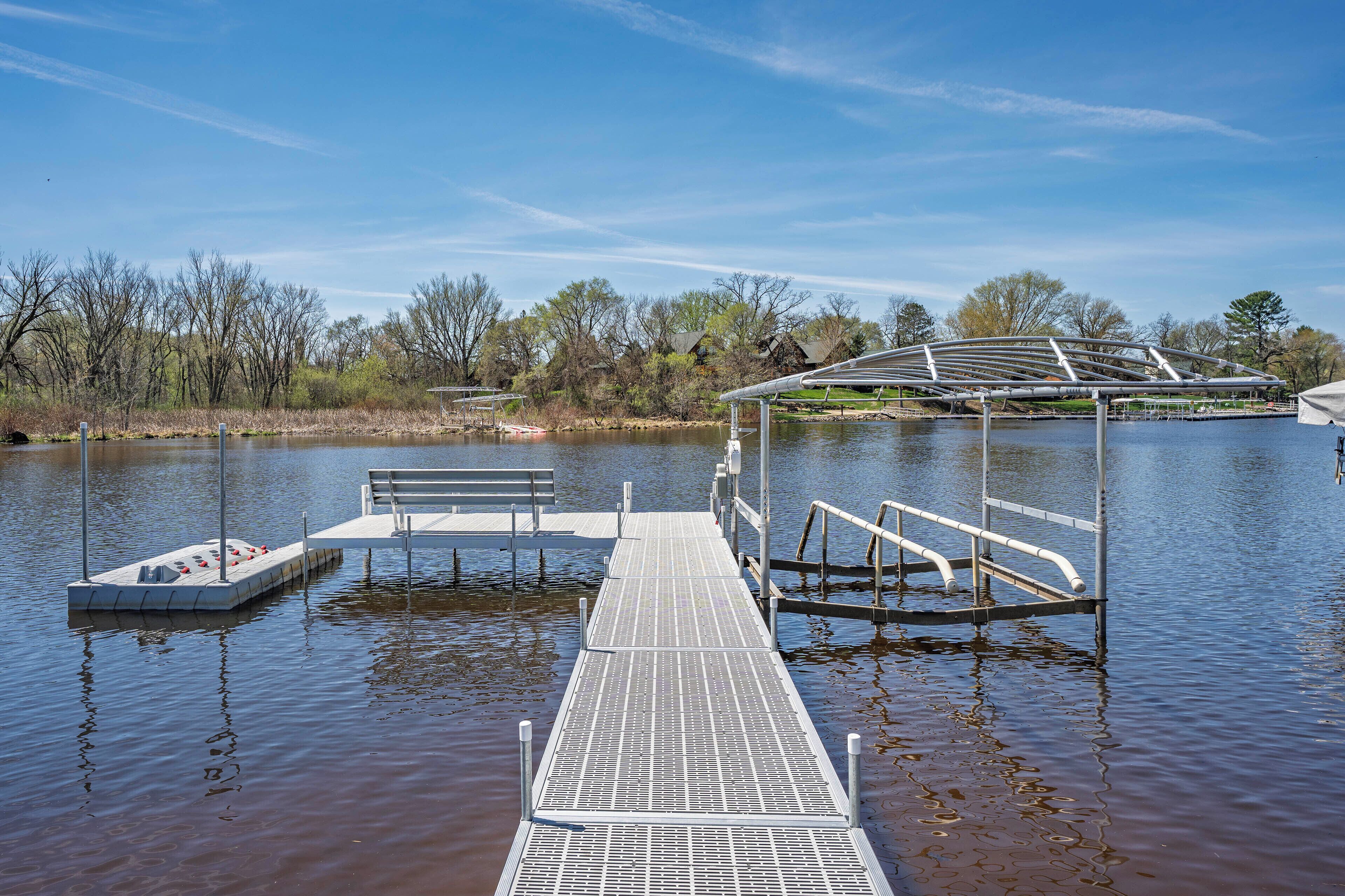 A pier extending into a calm body of water with a bench and a small boat docked nearby.