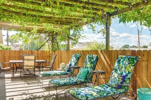Un patio al aire libre con una pérgola de madera, sillas de metal y una mesa.