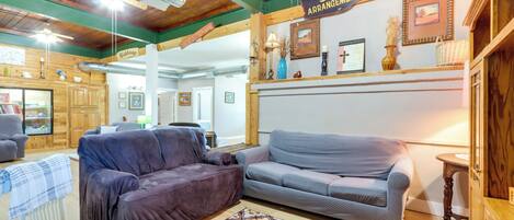 A cozy room with two sofas, a patterned rug, wooden beams, and a sign for 'Silk Arrangements'.