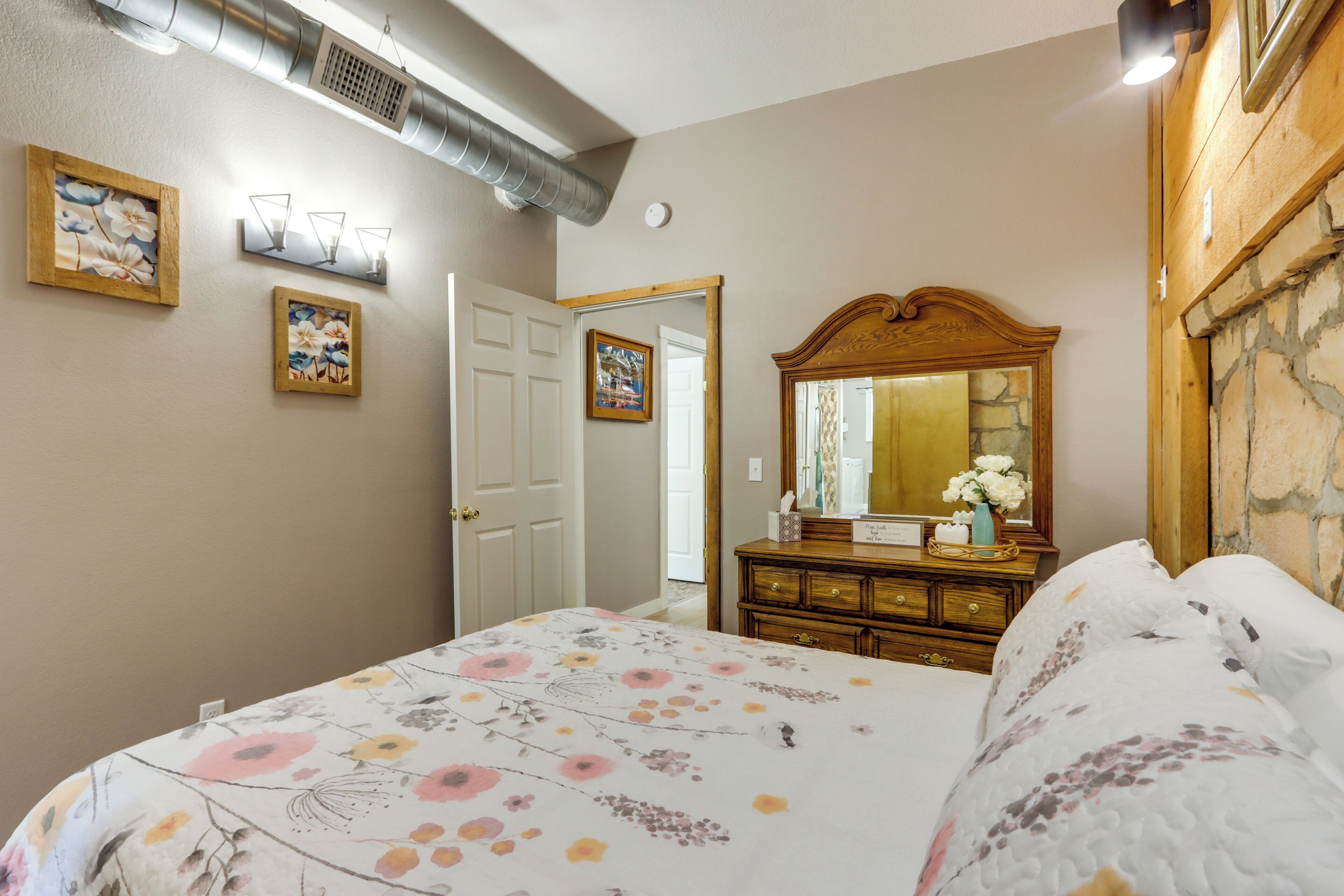 A bedroom with a bed, dresser, mirror, and artwork on the walls.