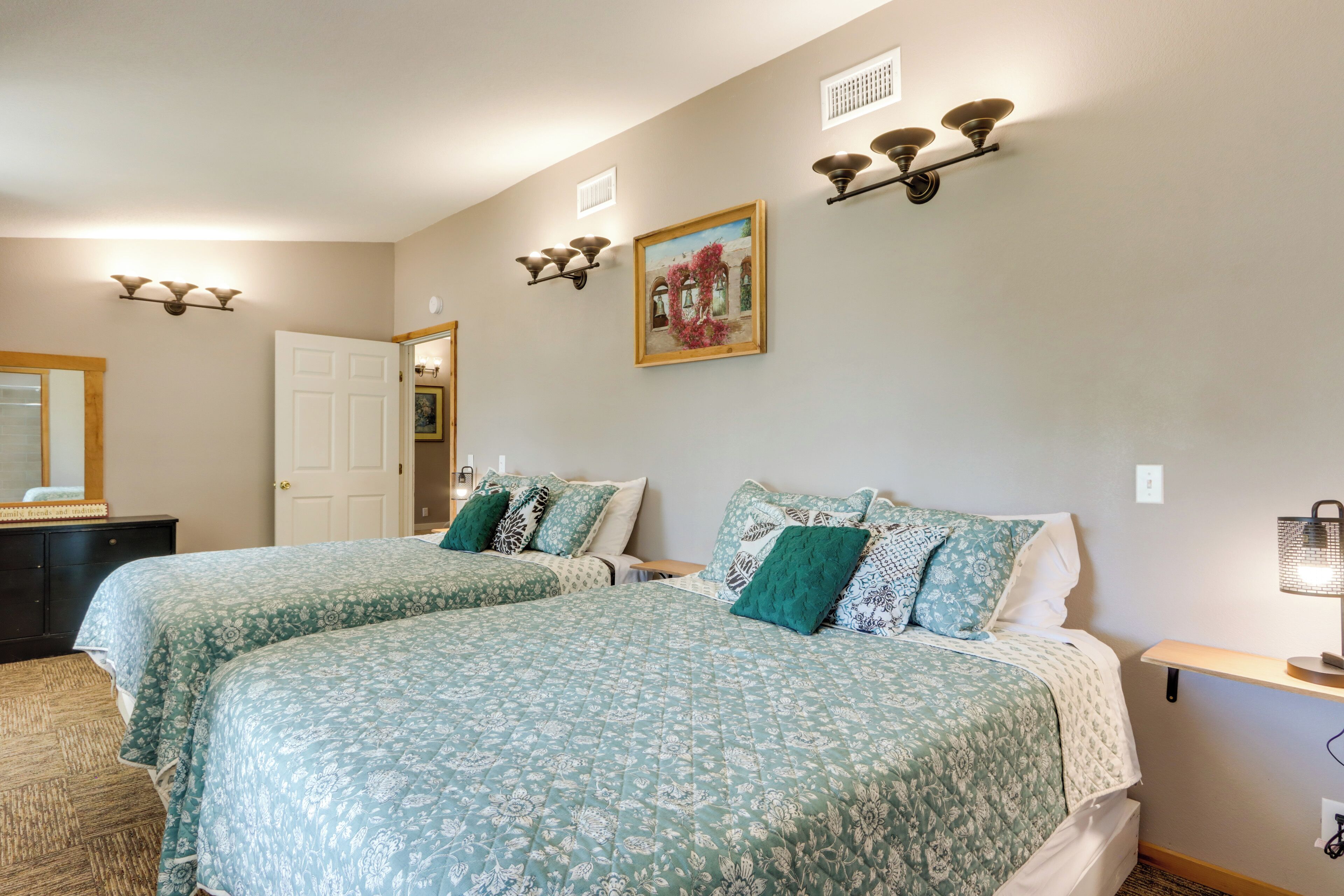 A bedroom with two beds, a dresser, a painting, and wall sconces.