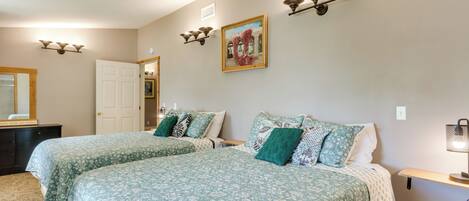 A bedroom with two beds, a dresser, a painting, and wall sconces.