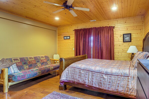 A wooden-paneled room with a bed, a sofa, and a ceiling fan. - Secluded Iowa Home Near Hiking & Fishing! (West Union)