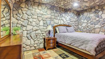 A bedroom with a stone wall, a bed with a quilt, a nightstand, and a mirror.