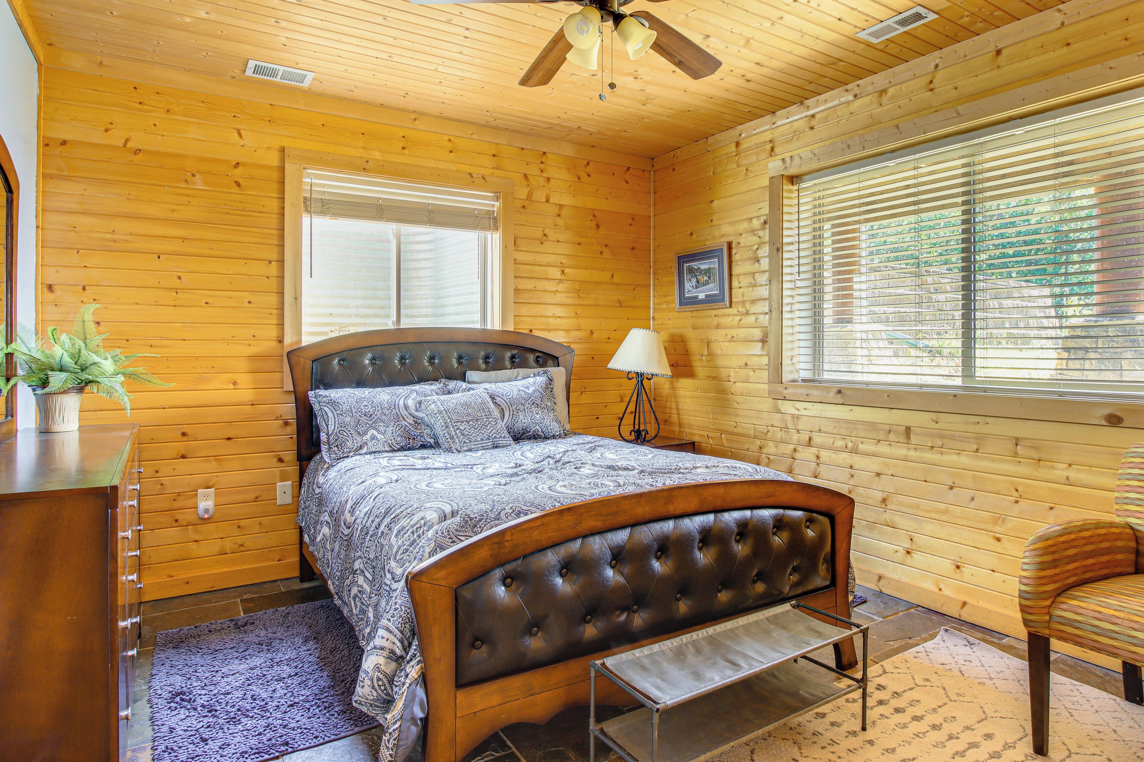 Une chambre à coucher dans une cabane en bois, avec un lit, une table de chevet, une lampe et une fenêtre avec des stores.