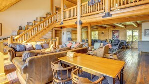 Un vaste espace de vie agrémenté d’un escalier en bois, de canapés en cuir, d’une table à manger et offrant une vue sur l’extérieur.