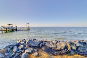 Eine felsige Küste mit einer hölzernen Pier, die sich in ruhiges Wasser erstreckt.
