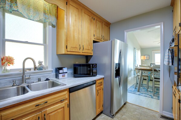 A kitchen with wooden cabinets, a stainless steel refrigerator, a microwave, and a double sink. - Pet-friendly Maryland Home on the Potomac River! (Leonardtown)