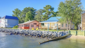 A waterfront property with a dock, a stone wall, and several buildings including a red house and a blue house. - Pet-friendly Maryland Home on the Potomac River! (Leonardtown)