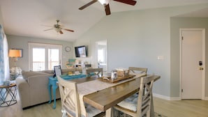 A dining area with a wooden table, chairs, and a ceiling fan. There is a sofa and a television in the background. - Pet-friendly Maryland Home on the Potomac River! (Leonardtown)