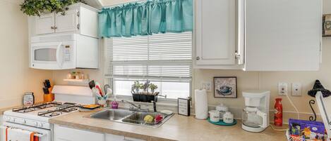 A kitchen with white cabinets, a microwave, a stove, a sink, and a window with blinds.