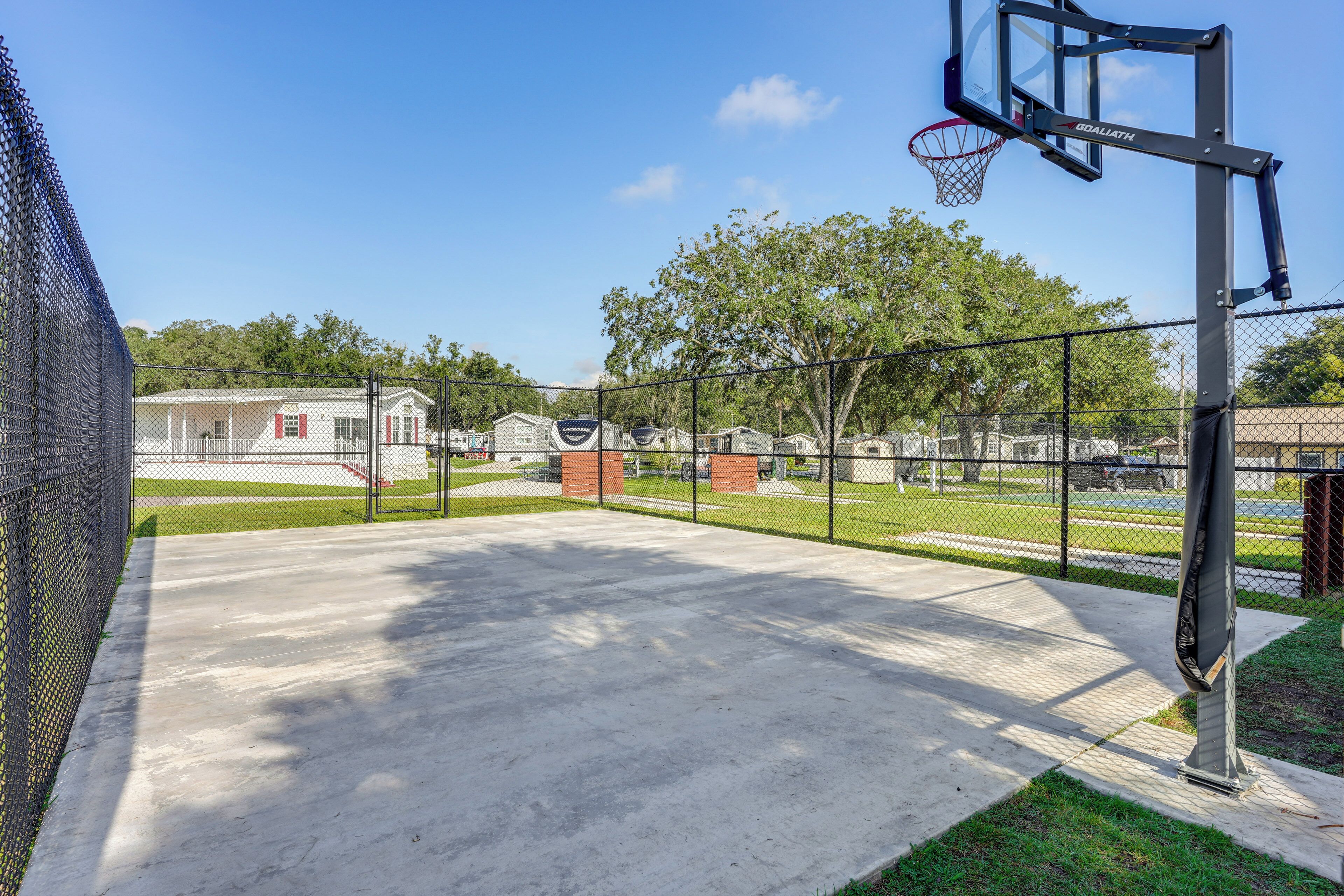 Una cancha de baloncesto al aire libre con una cerca de malla metálica, un aro de baloncesto y un edificio al fondo.