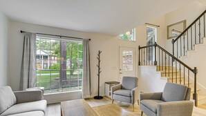 A spacious living room with a large window, a staircase, and a grey armchair. - Family Home w/ Game Room & Deck in Spring! (The Woodlands)
