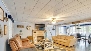 A cozy living room with a leather sofa, a wooden coffee table, and a beige couch. There's a fireplace with a stone surround, and the room has a nautical theme with anchors and a life preserver on the wall. - Dock w/ Deck & Waterslide: Lake of the Ozarks Gem! (Sunrise Beach)