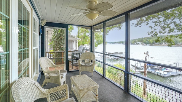 A covered balcony with wicker furniture, a ceiling fan, and a view of a lake with boats. - Dock w/ Deck & Waterslide: Lake of the Ozarks Gem! (Sunrise Beach)