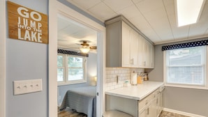 A compact kitchen with white cabinets, a countertop, and a ceiling fan. A sign on the wall reads "GO JUMP INTO THE LAKE." - Dock w/ Deck & Waterslide: Lake of the Ozarks Gem! (Sunrise Beach)