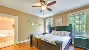 A bedroom with a large bed, a ceiling fan, a window with a view, and a bathroom with a bathtub and toilet. - Fire Pit, Large Yard: Midtown Columbus Bungalow! (Columbus)
