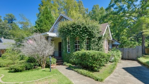 A single-story house with a front porch, surrounded by lush greenery and a wooden fence. - Fire Pit, Large Yard: Midtown Columbus Bungalow! (Columbus)