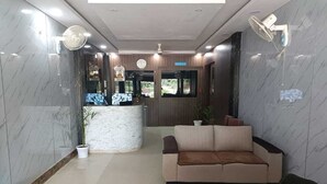 A lobby with a reception desk, a sofa, a fan, and a clock on the wall. - HOTEL CORPORATE INN (Supaul)