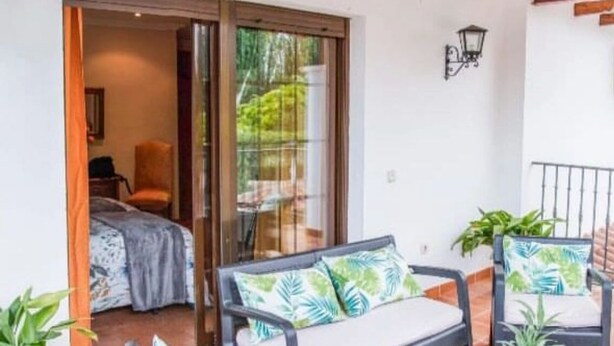 A patio with two black chairs and a table, a sliding glass door leading to a bedroom, and a potted plant. - Perfect for your meetings, adequate space, beautiful, functional, well equipped. (Urda)