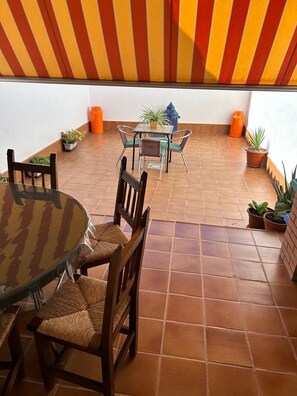 Une terrasse avec une table ronde et des chaises, une petite table carrée avec des chaises, et des plantes en pot.