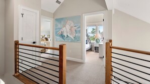 A staircase with wooden railings leading to a bedroom with a large seashell painting. - Exhale: Renovated, Hot Tub, Golf Course Views (Nags Head)