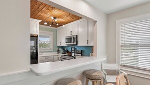 A modern kitchen with white cabinets, a wooden ceiling, and a bar area with stools. - Exhale: Renovated, Hot Tub, Golf Course Views (Nags Head)
