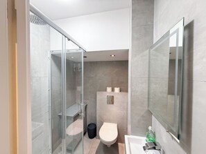 Un baño moderno con ducha de vidrio, inodoro y lavamanos con espejo.