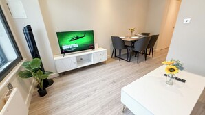 A modern living room with a flat-screen TV, a dining area with a table and chairs, and a small plant on the windowsill. - London's 1-Bedroom Haven near The Shard in Elephant & Castle (London)