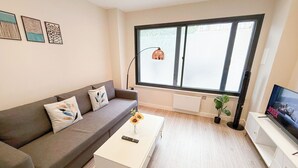 A modern living room with a grey sofa, a white coffee table, and a TV on a white cabinet. - London's 1-Bedroom Haven near The Shard in Elephant & Castle (London)